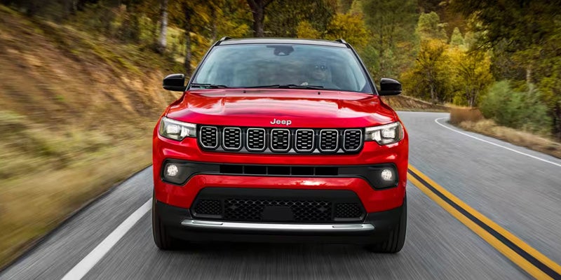 Red Jeep Compass SUV driving on a road surrounded by forest.