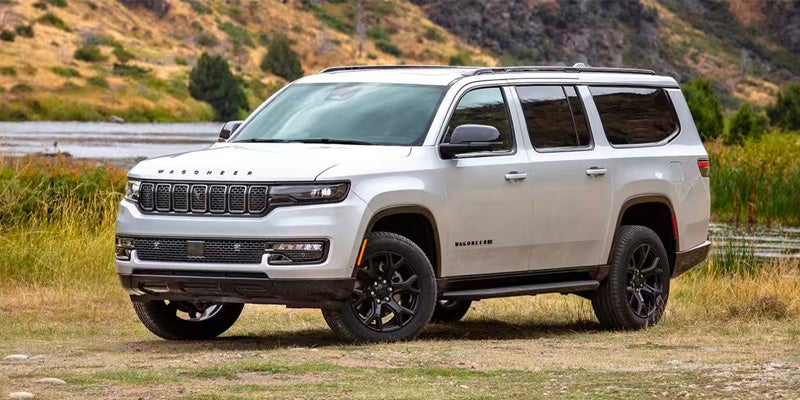 White Jeep Wagoneer L SUV parked near a grassy riverbank