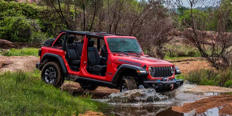 Red Jeep Wrangler off-roading in a stream